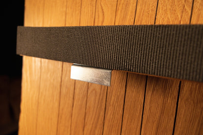 Detailed close-up view of a polished metal mounting clip securing the textured fabric strap against the vertical solid oak slats.