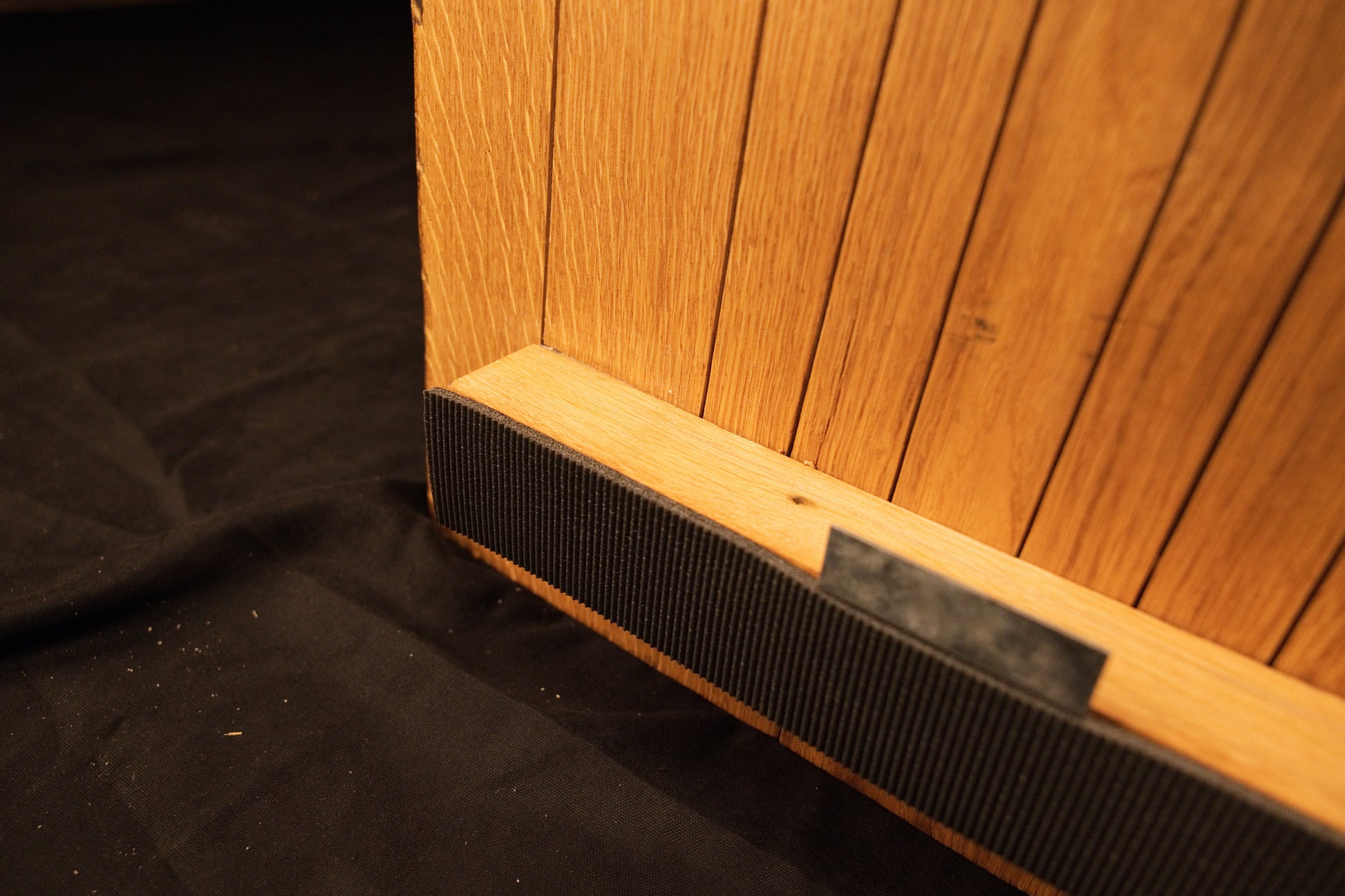 Close-up view of the lower horizontal mounting bracket securely fastened across the bottom edge of the vertical oak panel slats.