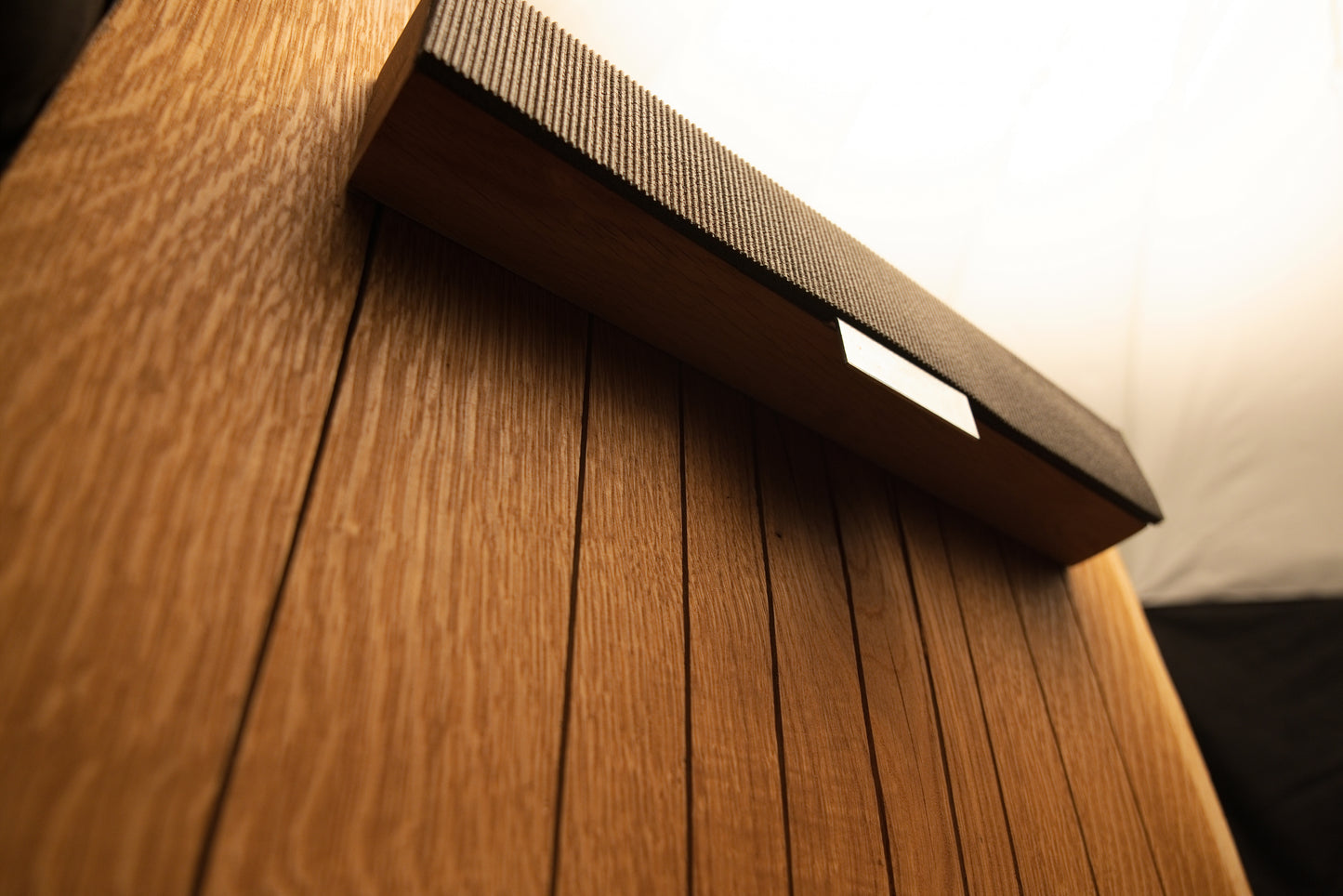 Angled side perspective of the lower horizontal mounting bracket wrapped in dark fabric against the vertical oak slats.