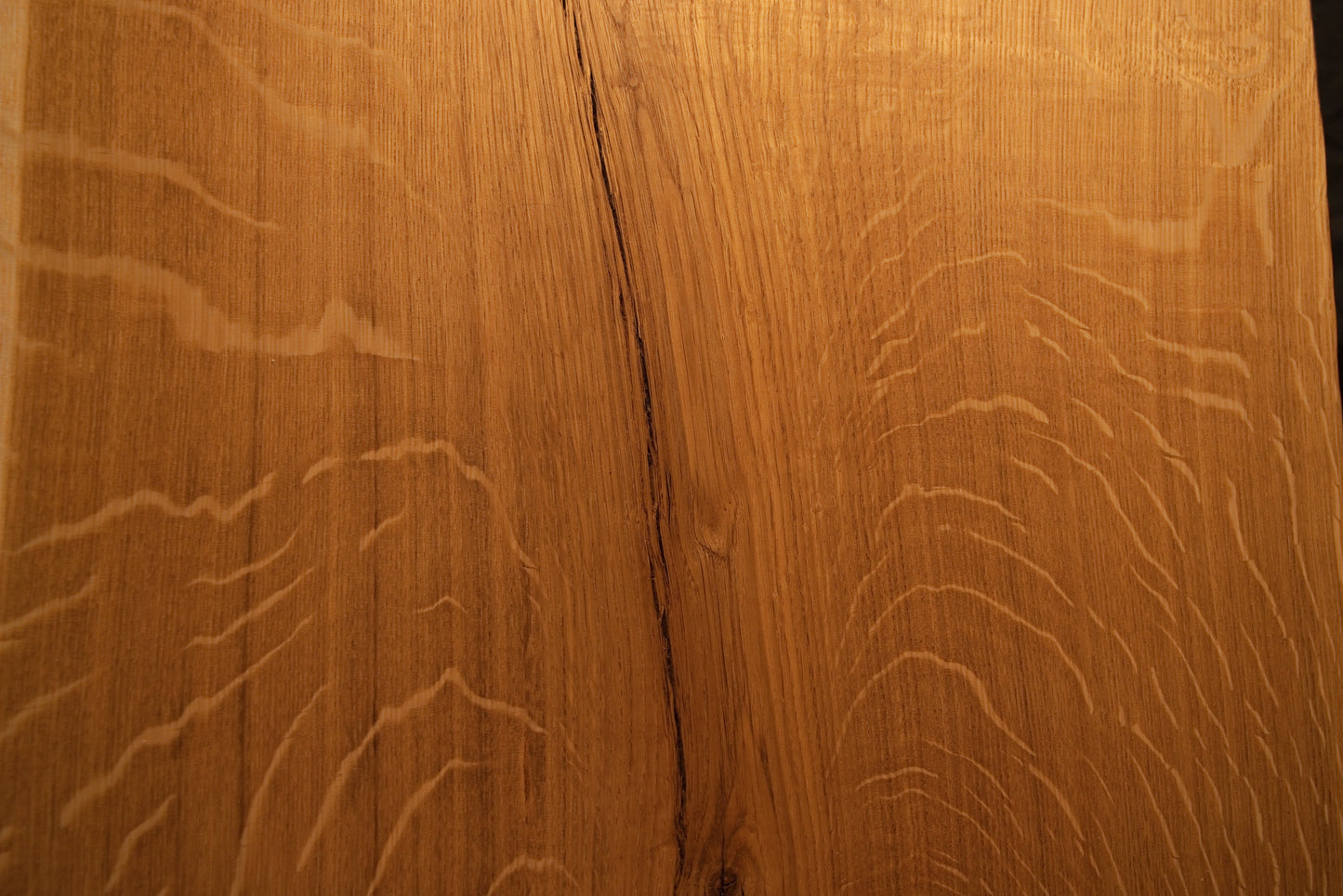 Detailed macro focus on the intersection between fine vertical wood grain and sweeping medullary ray reflections on the oak slab.