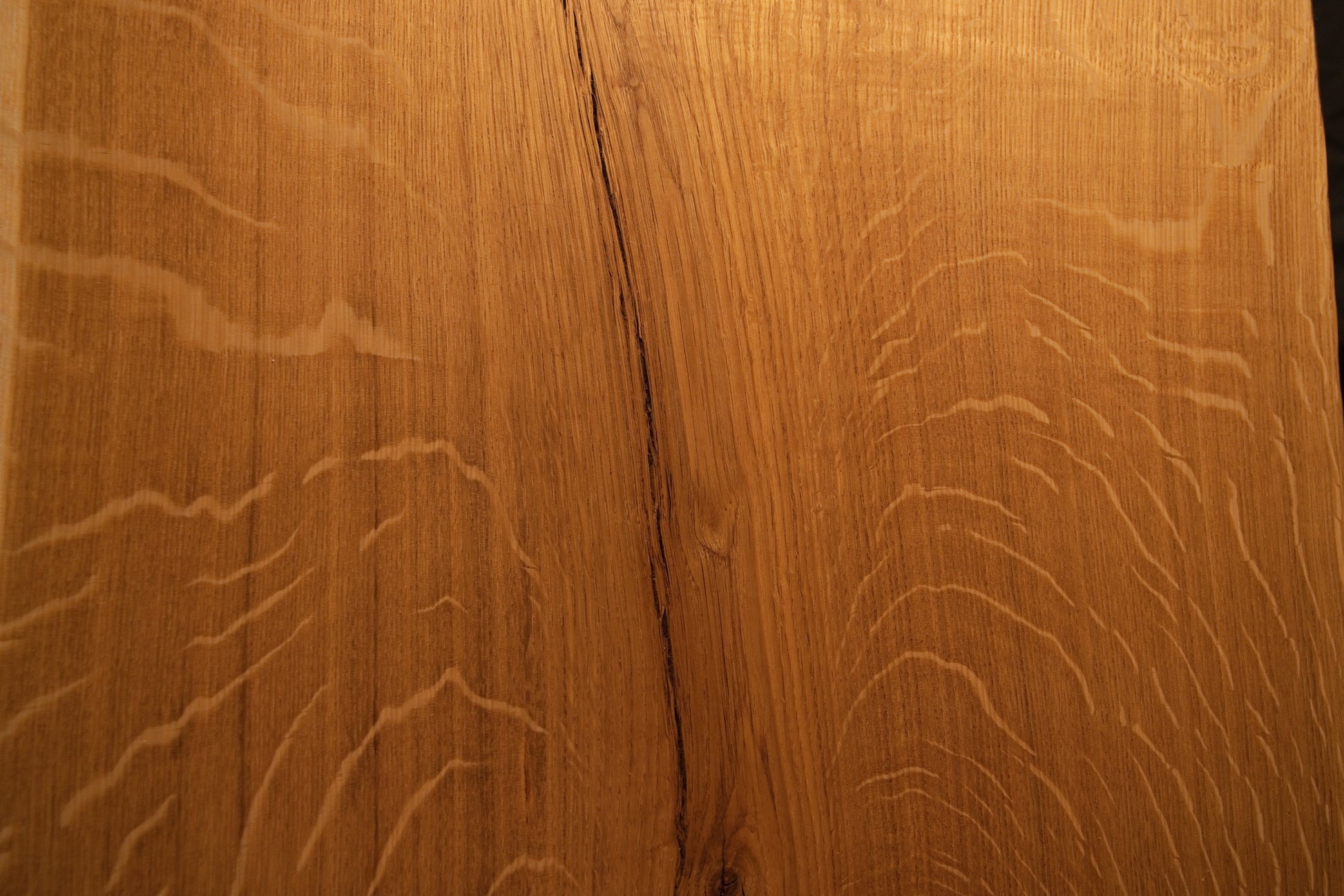 Detailed macro focus on the intersection between fine vertical wood grain and sweeping medullary ray reflections on the oak slab.