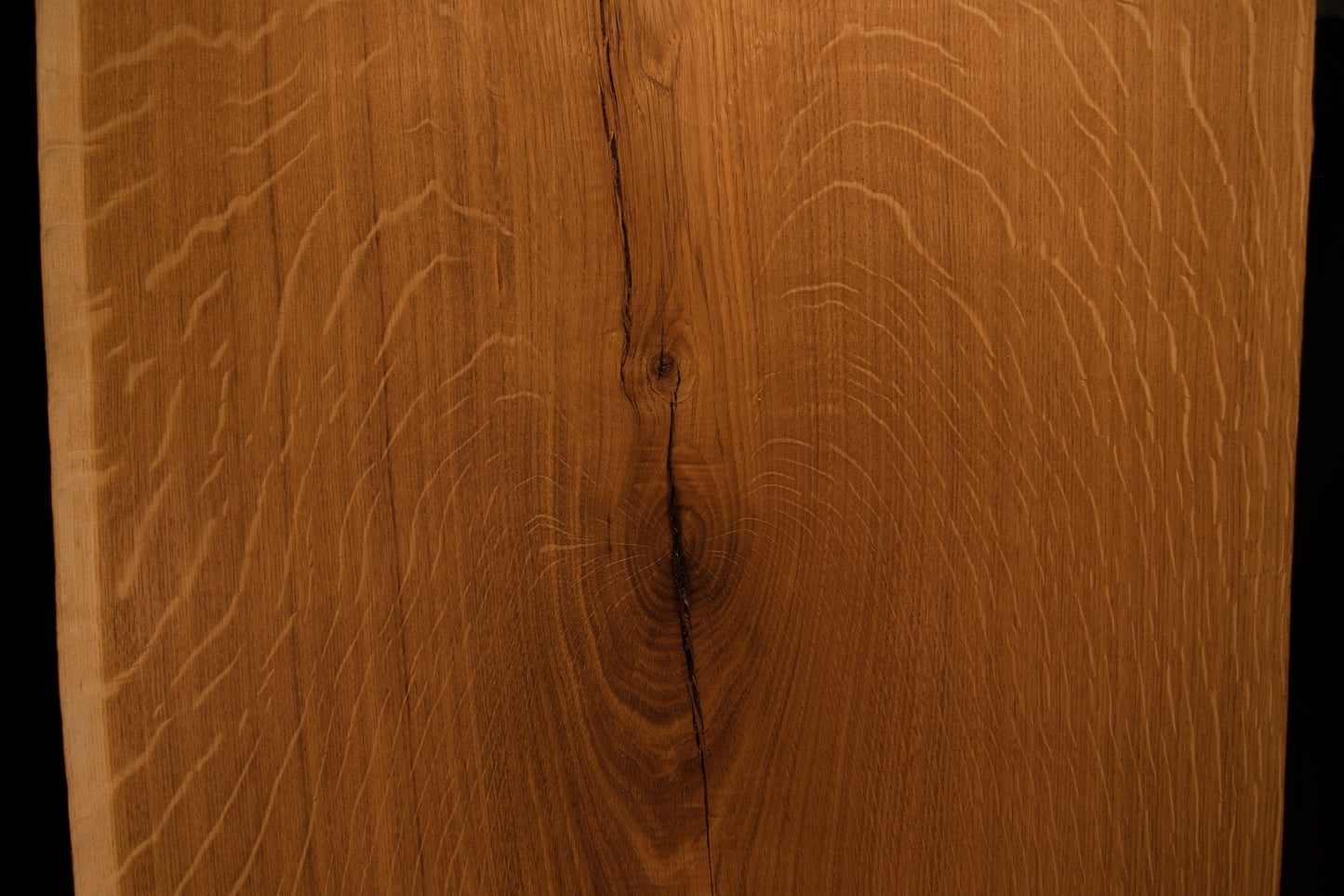 Close-up macro showing a natural wood knot splitting into a delicate fissure across the highly figured solid oak wooden panel face.