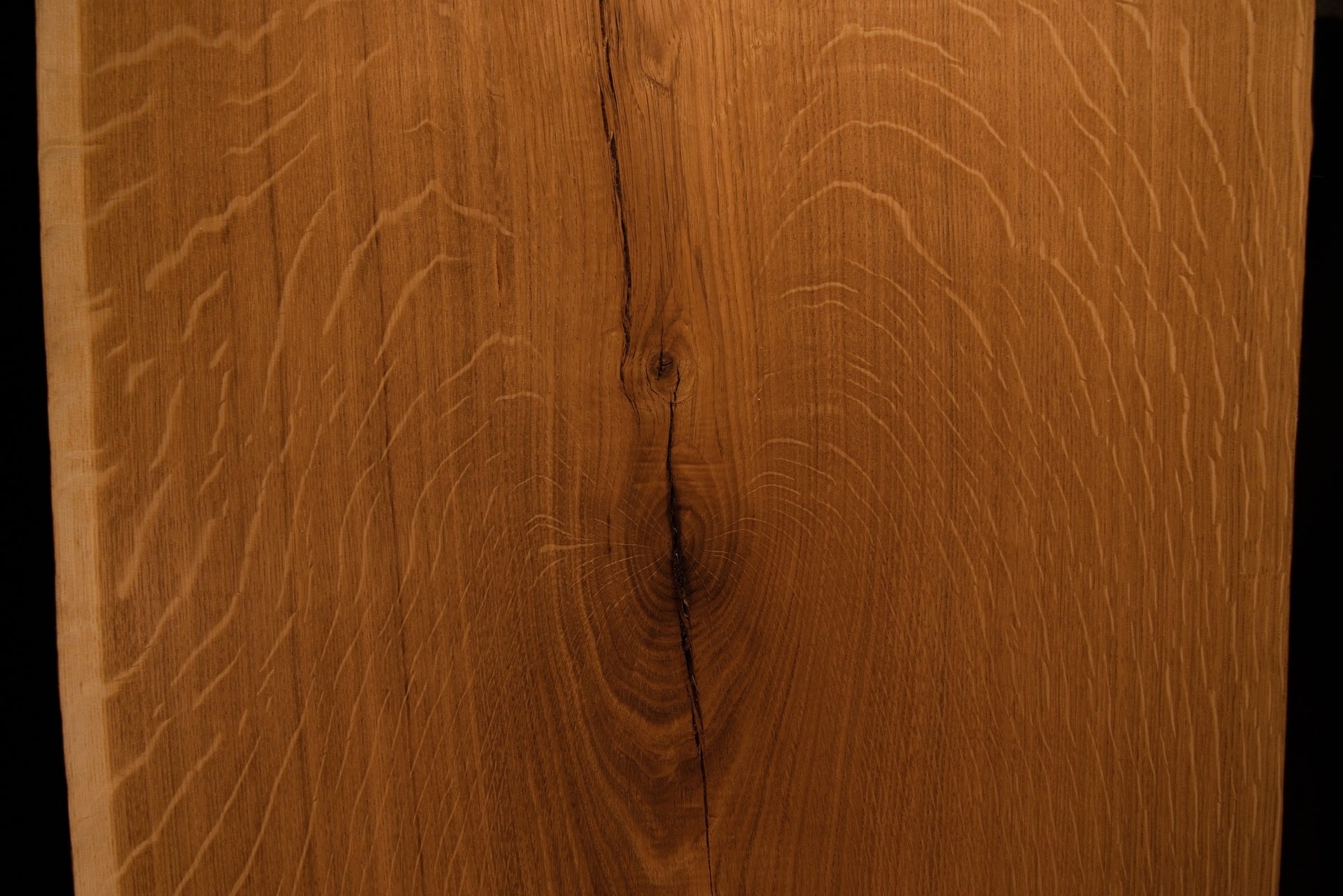 Close-up macro showing a natural wood knot splitting into a delicate fissure across the highly figured solid oak wooden panel face.