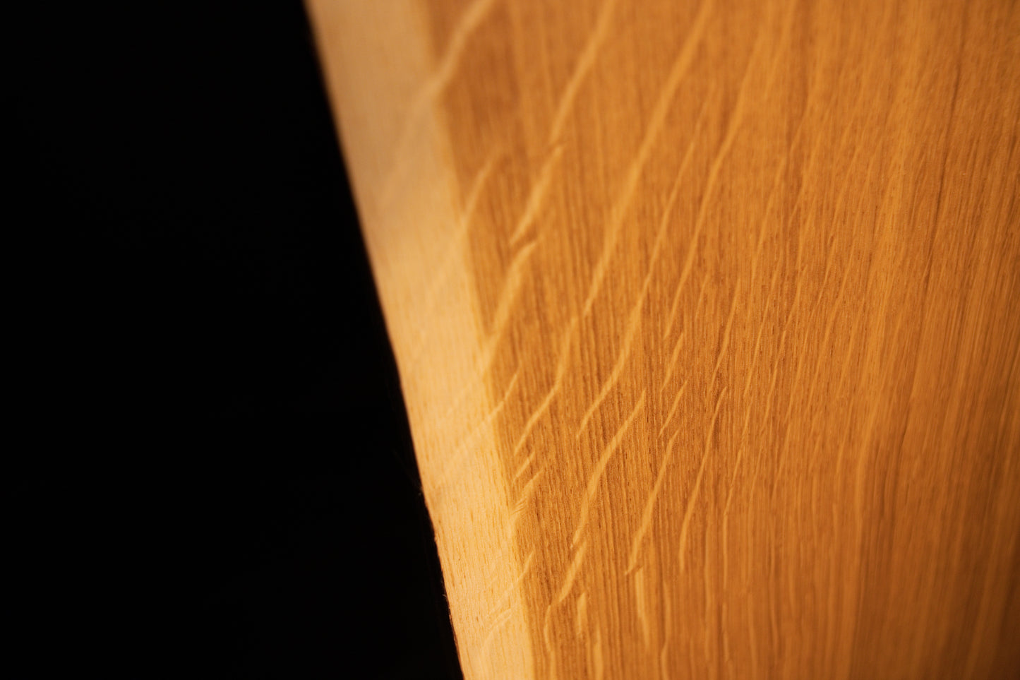 Detailed extreme close-up of shimmering medullary rays catching the light along the angled side edge of the custom solid oak wood panel.