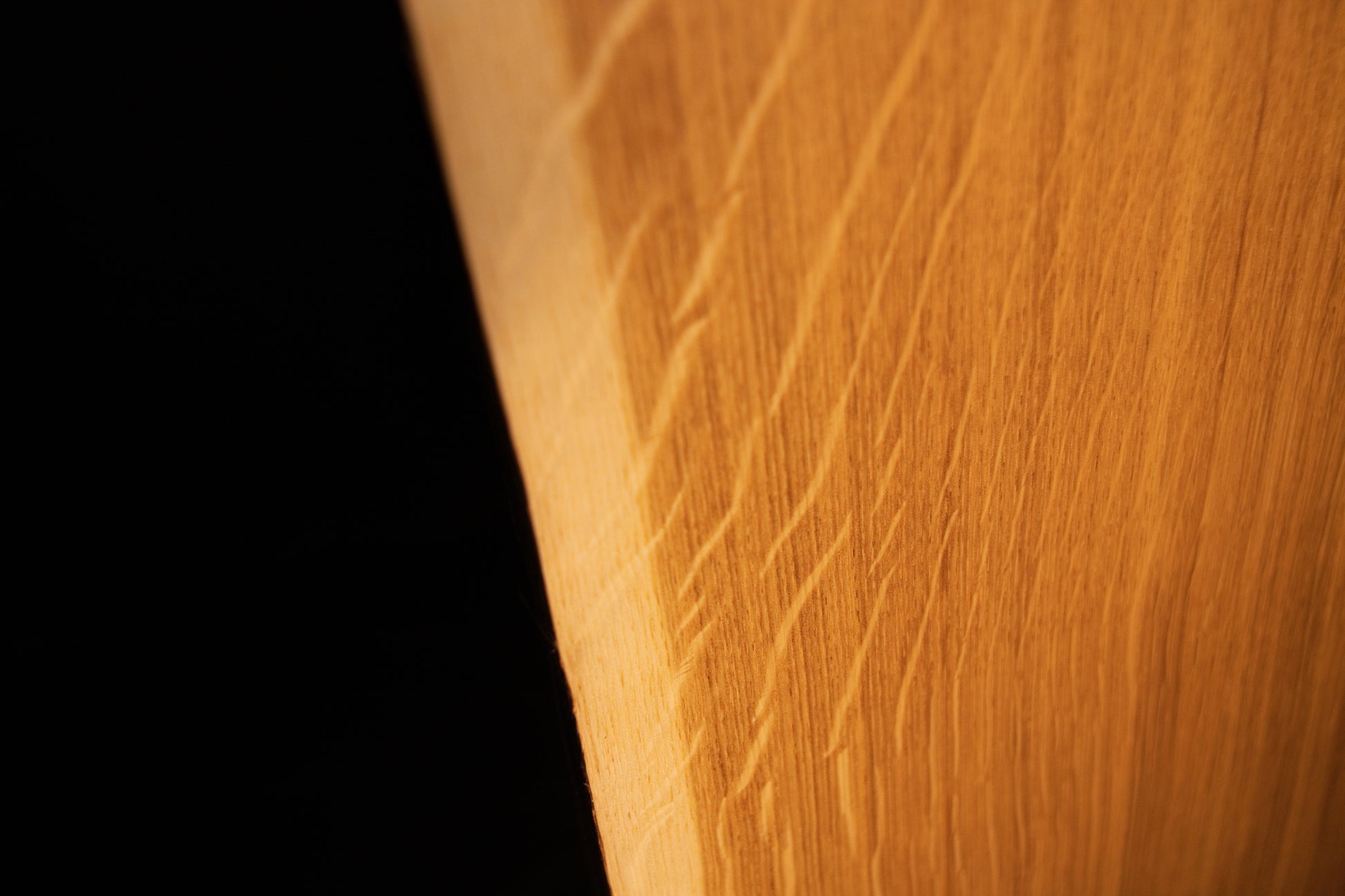 Detailed extreme close-up of shimmering medullary rays catching the light along the angled side edge of the custom solid oak wood panel.