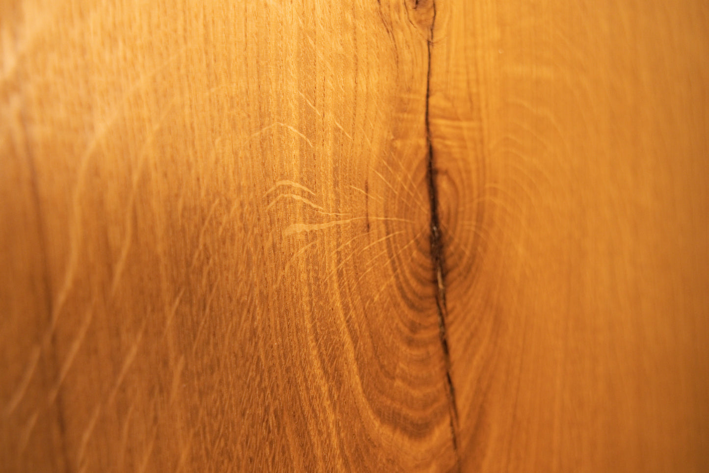 Macro view of an organic wood knot surrounded by expanding rippling grain patterns on the custom solid oak architectural piece.