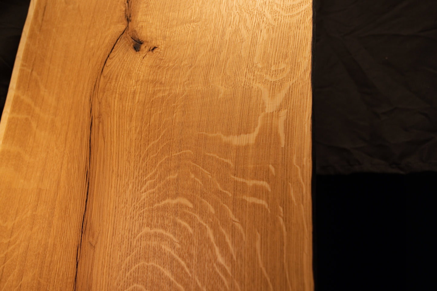 Close-up view of shimmering chatoyant medullary rays shifting across the warm golden surface of the custom architectural oak panel.