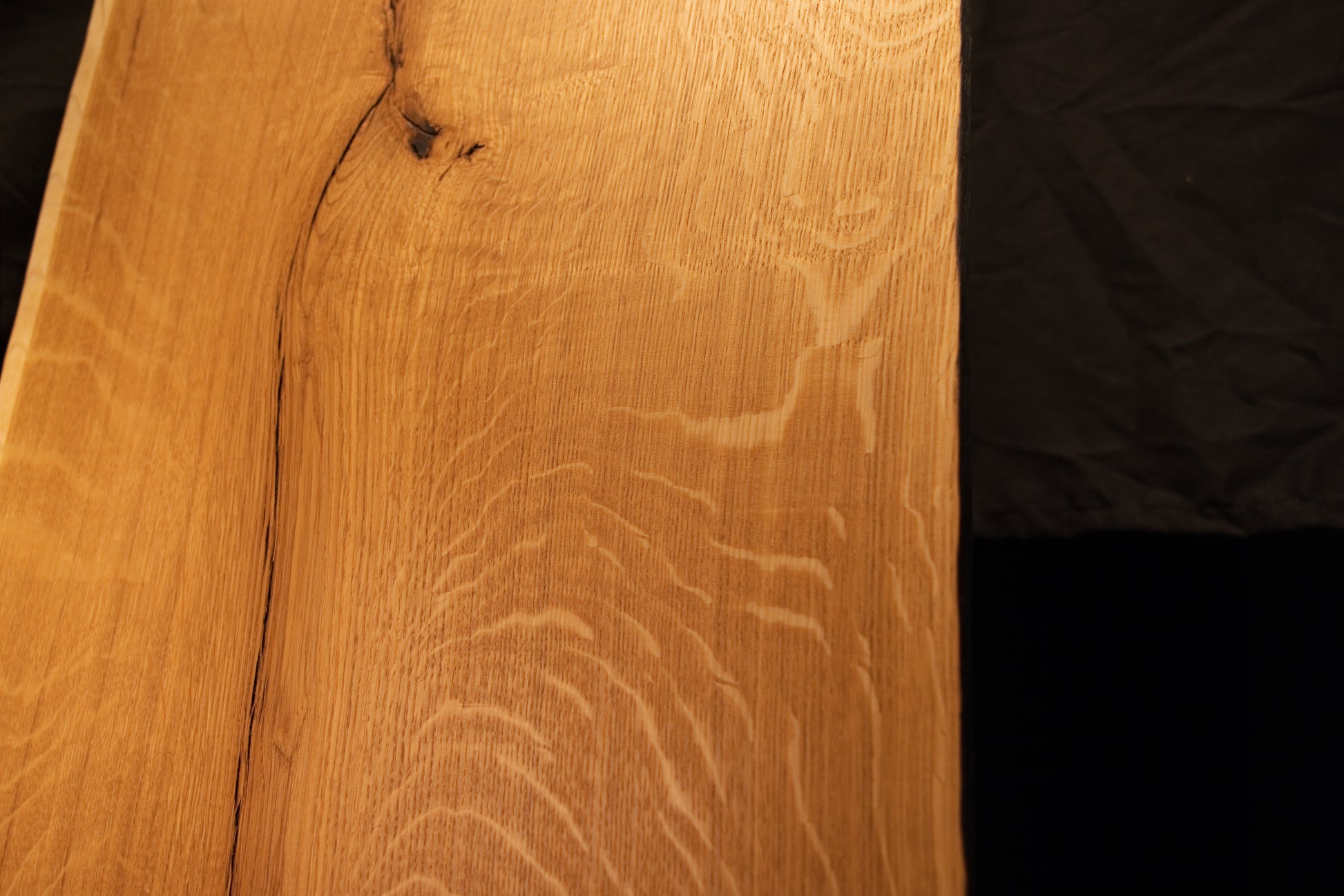 Close-up view of shimmering chatoyant medullary rays shifting across the warm golden surface of the custom architectural oak panel.