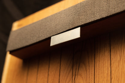Detailed close-up view of a polished metal mounting clip securing the textured fabric strap against the vertical oak slats. 