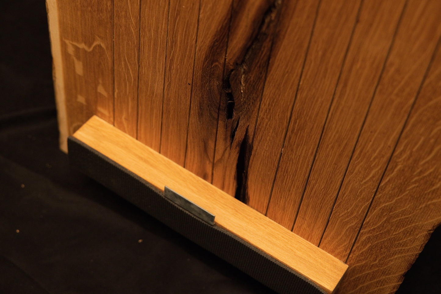 Close-up view of the lower horizontal mounting bracket securely fastened across the bottom edge of the vertical oak panel slats. 