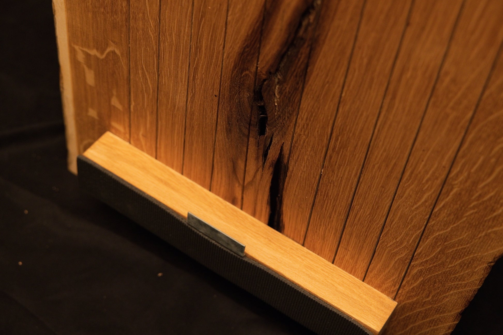 Close-up view of the lower horizontal mounting bracket securely fastened across the bottom edge of the vertical oak panel slats. 