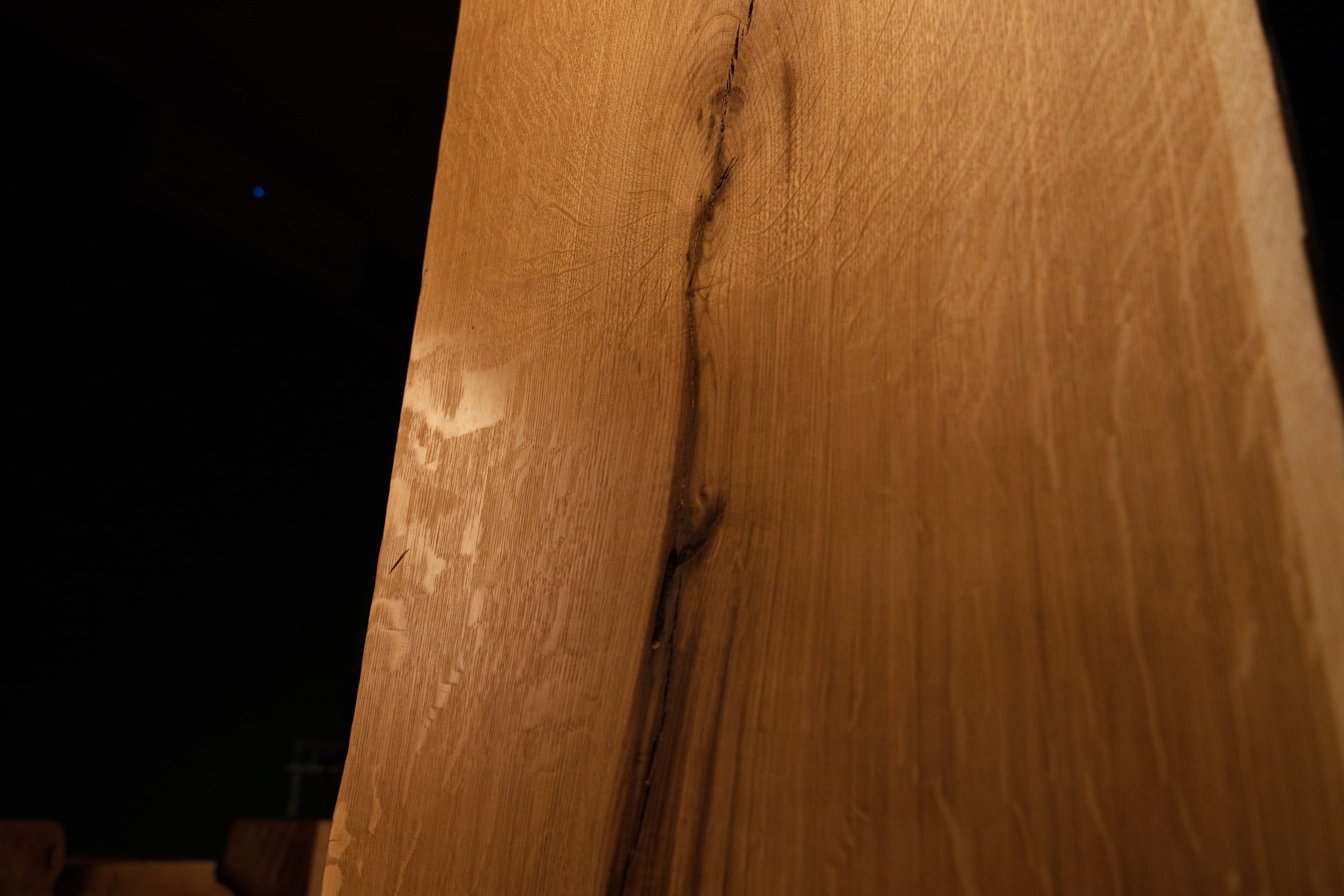 Detailed macro focus on the intersection between fine vertical wood grain and sweeping medullary ray reflections on the slab. 