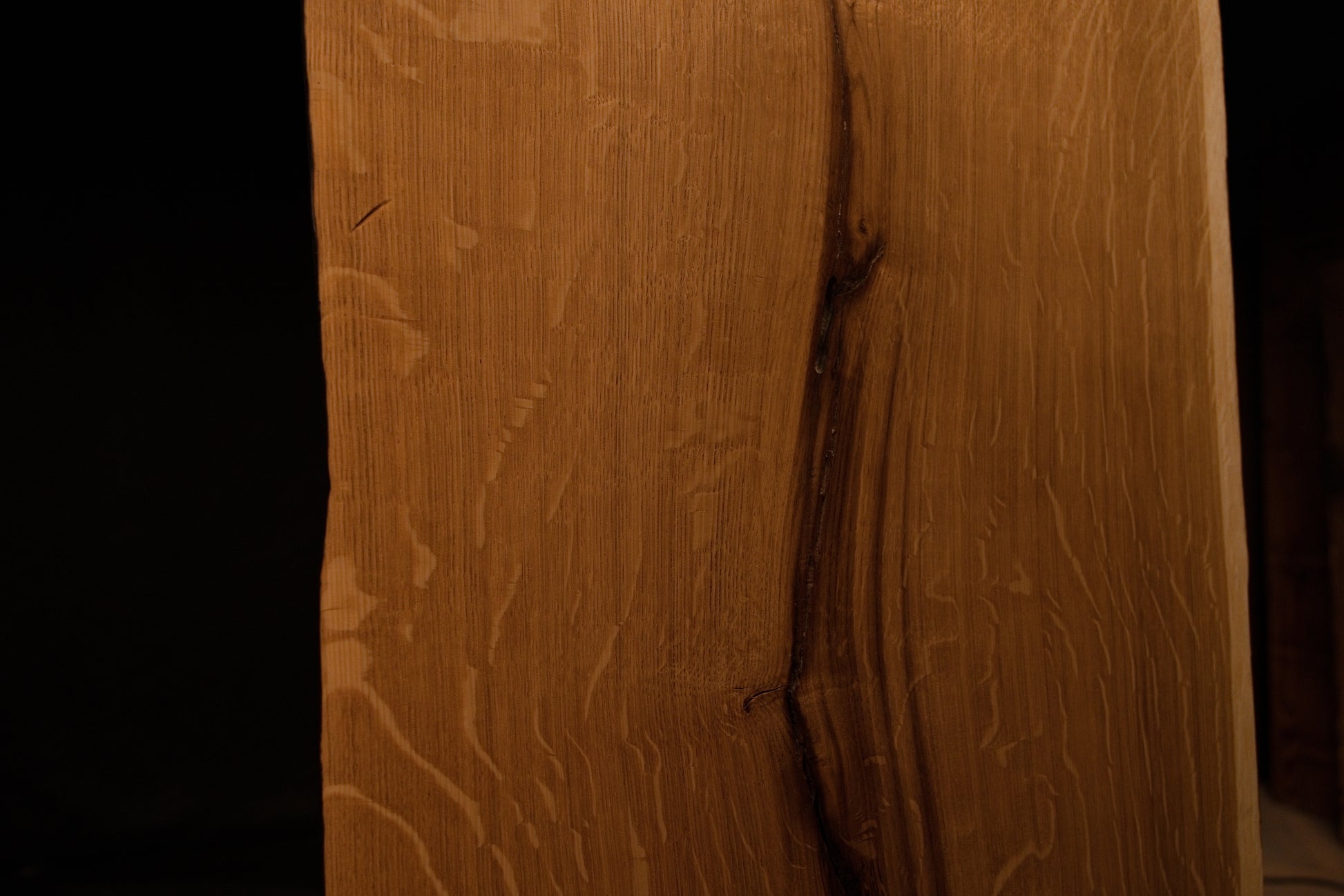 Macro close-up of vertical wood fibers and subtle grain variations along the polished outer edge of the solid oak board. 