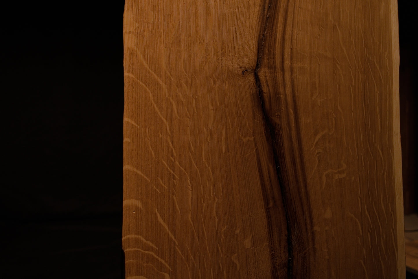 Detailed extreme close-up of shimmering medullary rays catching light along the angled side edge of the custom solid oak panel. 