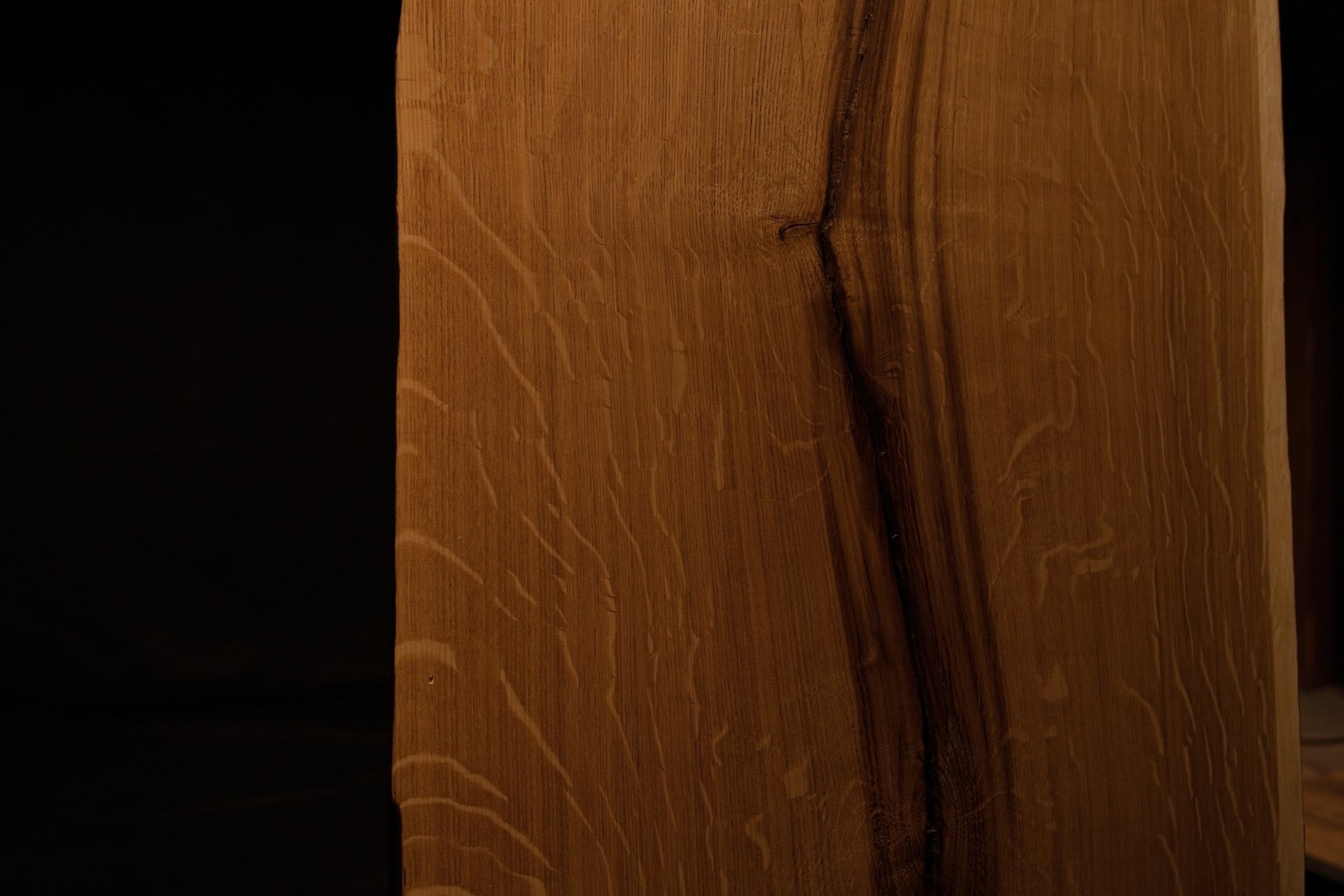 Detailed extreme close-up of shimmering medullary rays catching light along the angled side edge of the custom solid oak panel. 