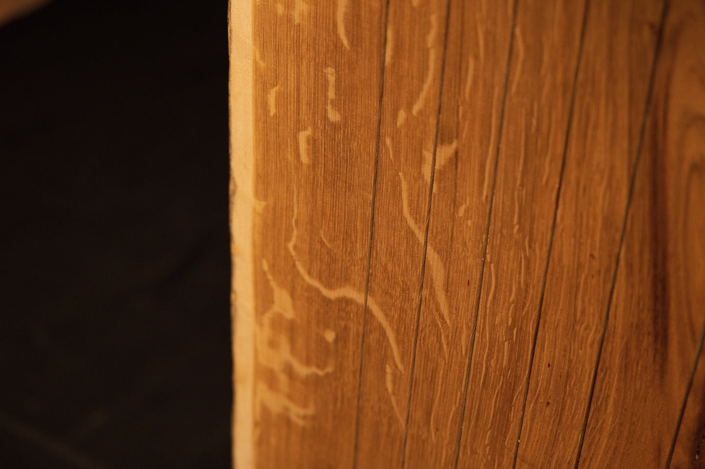 Detailed macro view of delicate insect trails or wormholes etched into the warm golden grain of the solid oak surface. 