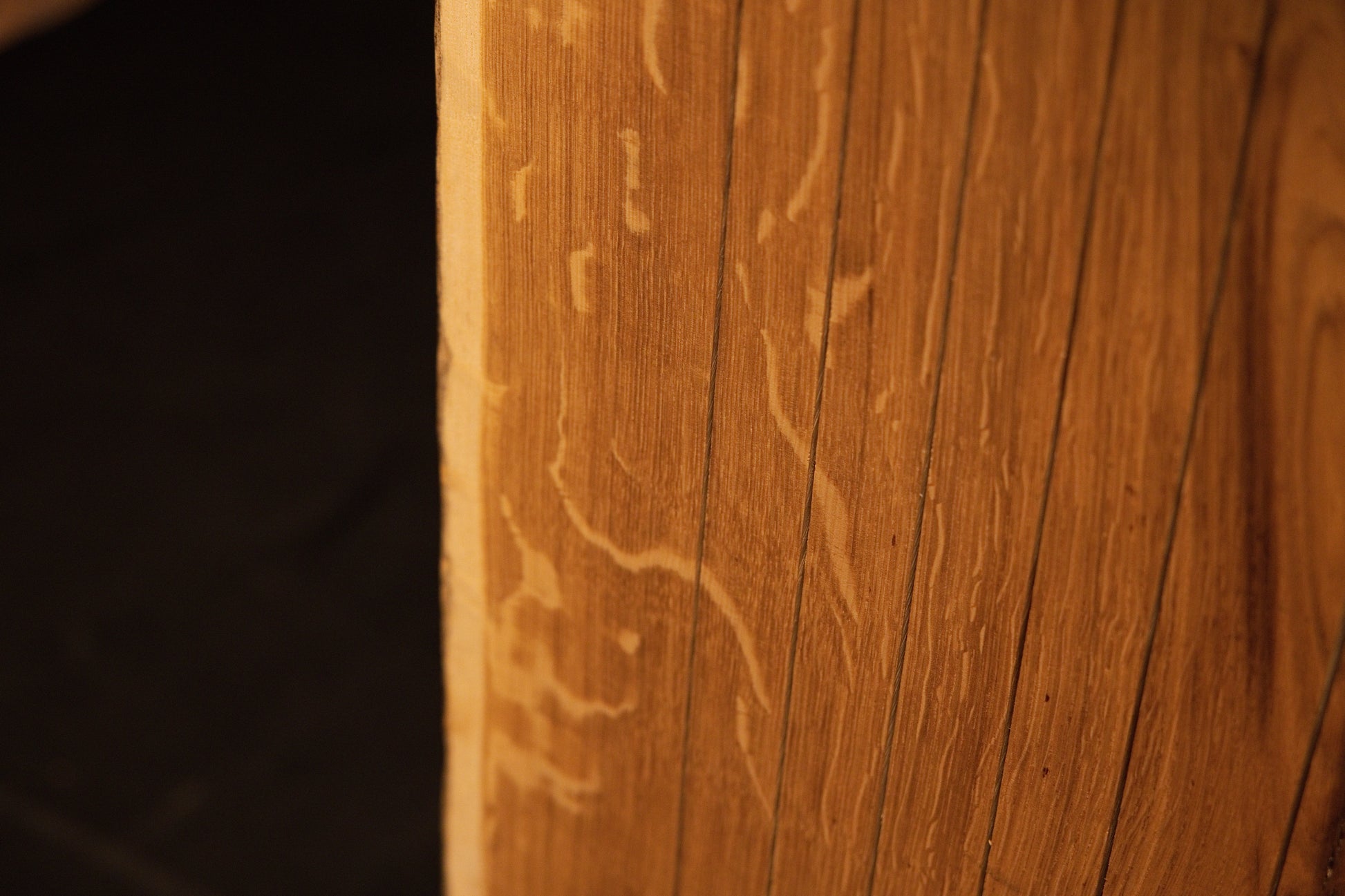 Detailed macro view of delicate insect trails or wormholes etched into the warm golden grain of the solid oak surface. 