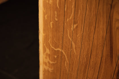 Detailed macro view of delicate insect trails or wormholes etched into the warm golden grain of the solid oak surface. 
