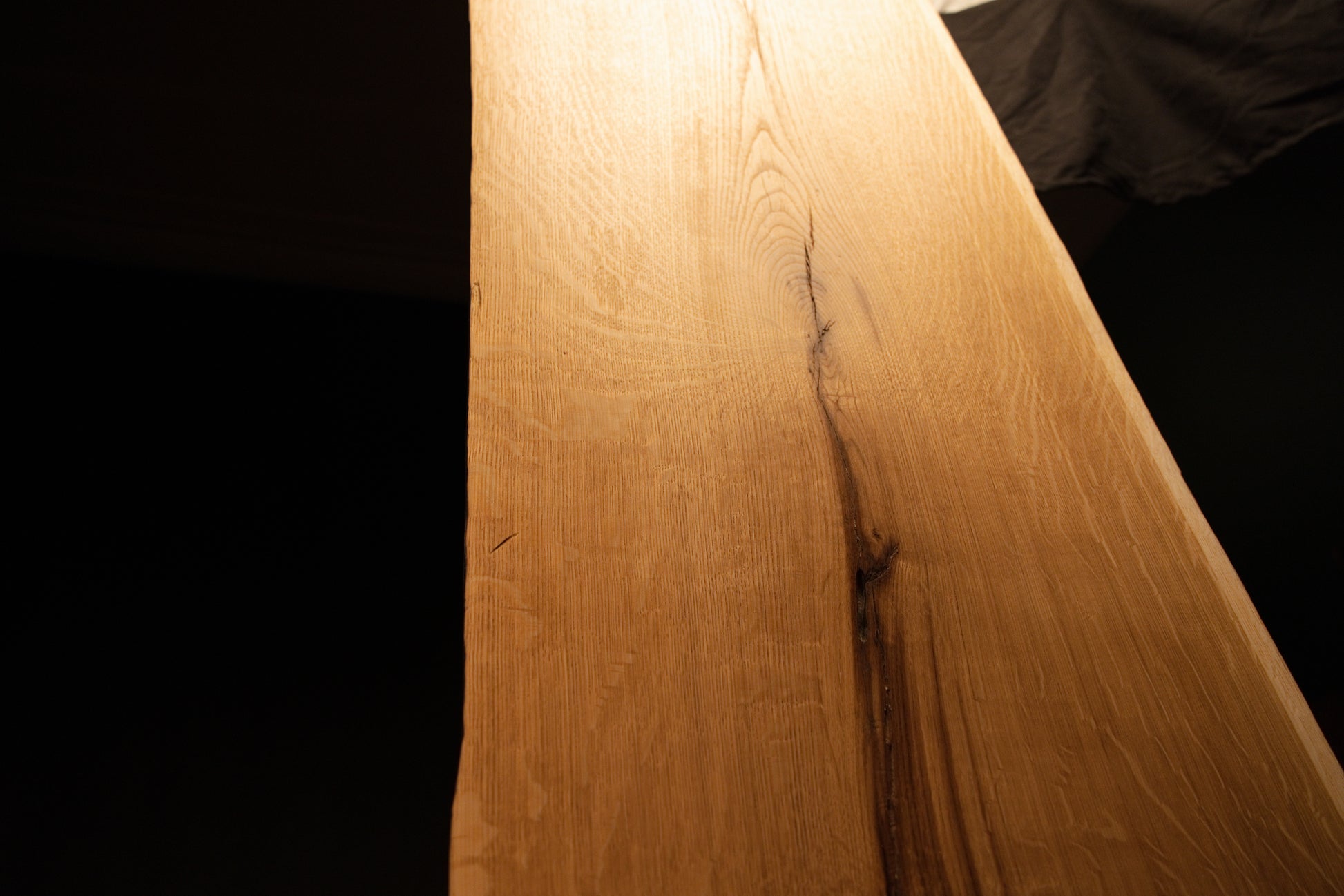 Angled close-up view tracing a dark natural fissure running down the length of the highly figured solid oak mirror board. 