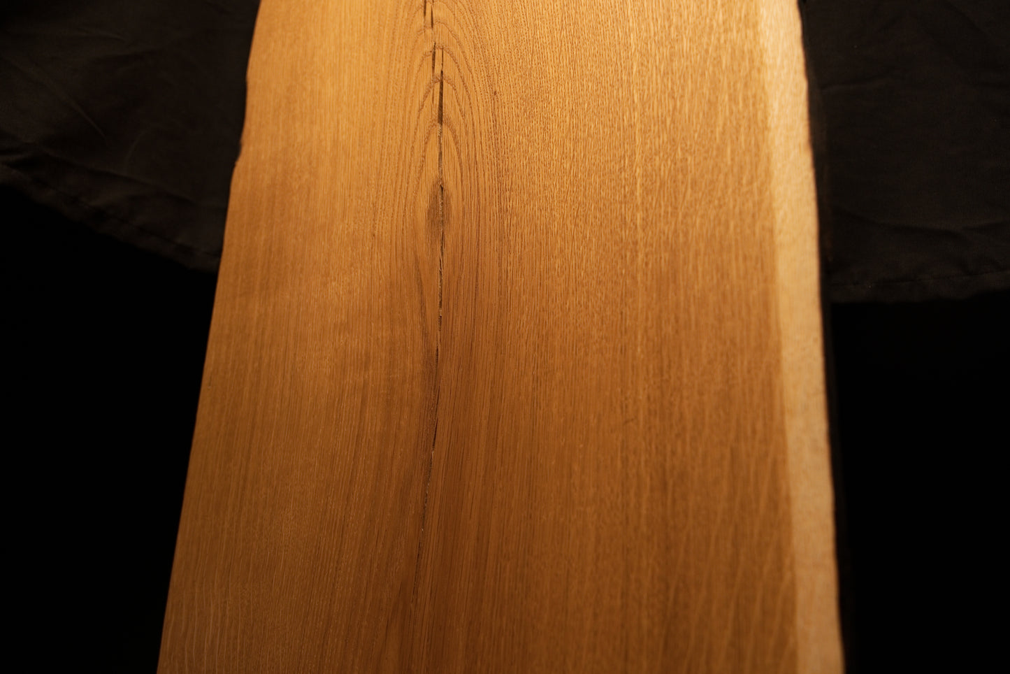 Close-up macro perspective of fine linear wood grain and smooth surface contours near the upper center of the oak board. 