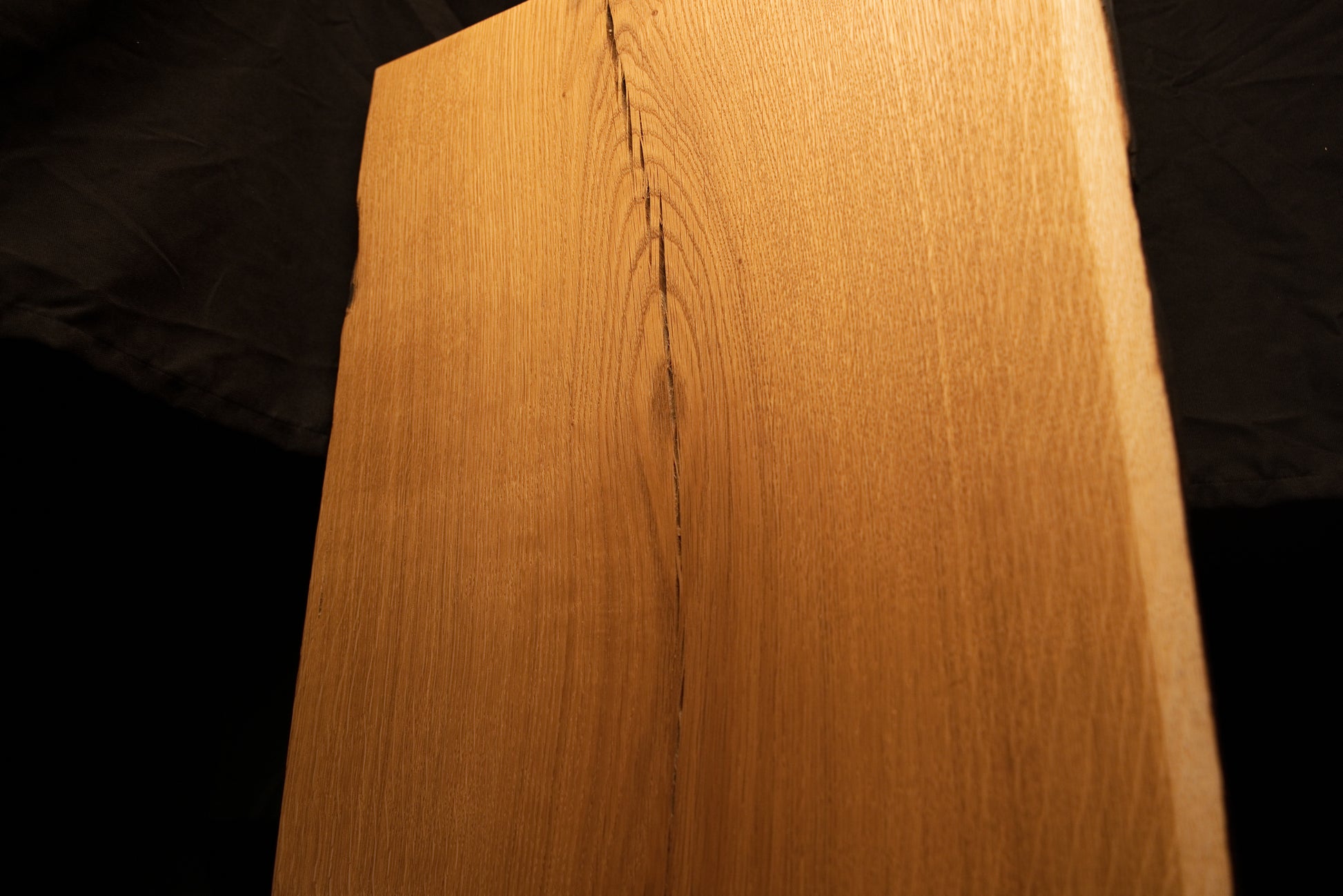 Close-up photograph of prominent parabolic grain curves opening up around a tight vertical split near the upper oak edge. 