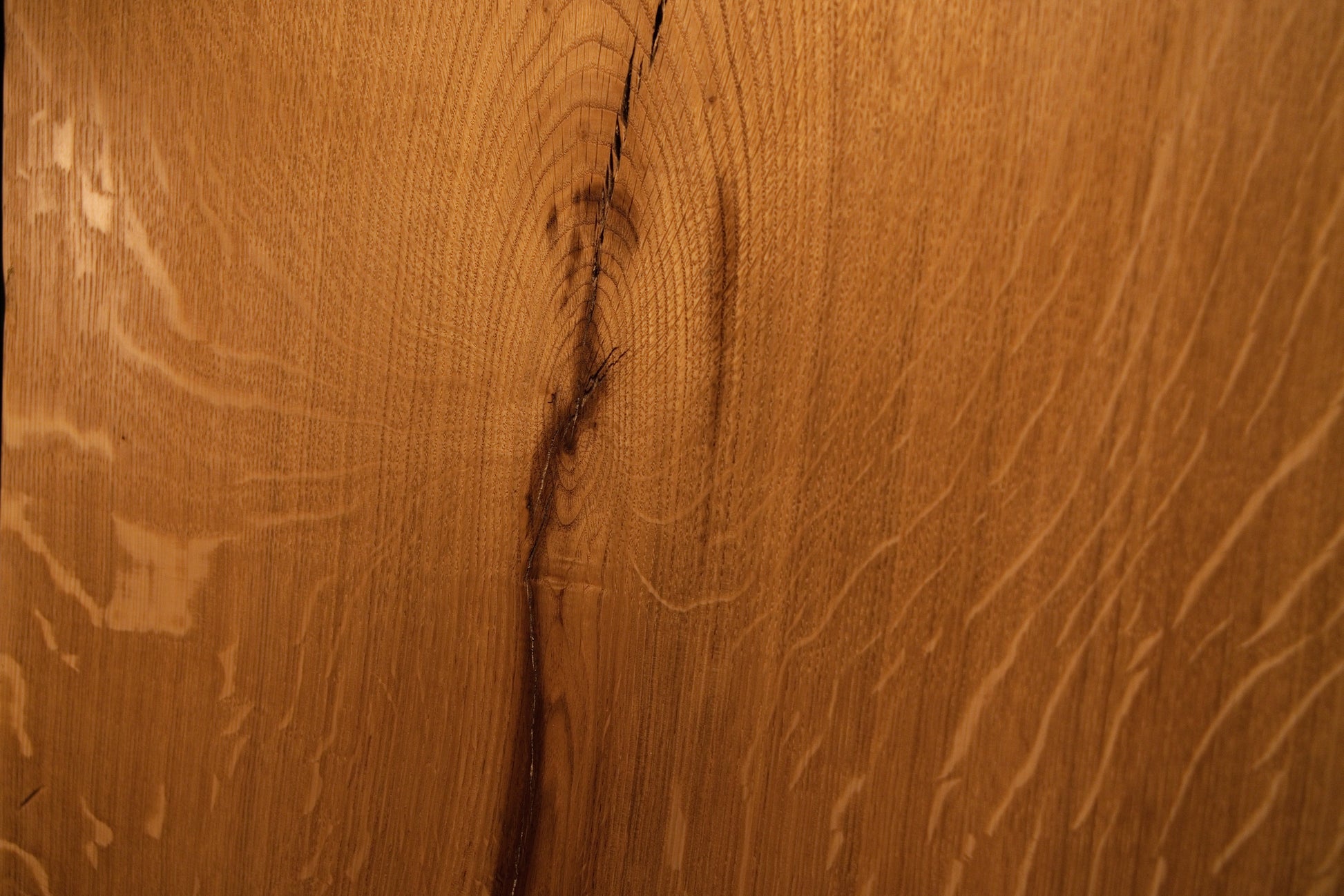 Detailed extreme close-up of a dark natural knot splitting into an organic fissure across the solid oak architectural board. 