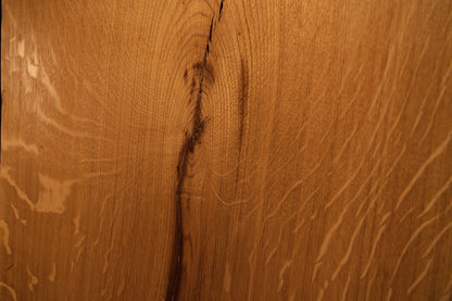 Detailed extreme close-up of a dark natural knot splitting into an organic fissure across the solid oak architectural board. 