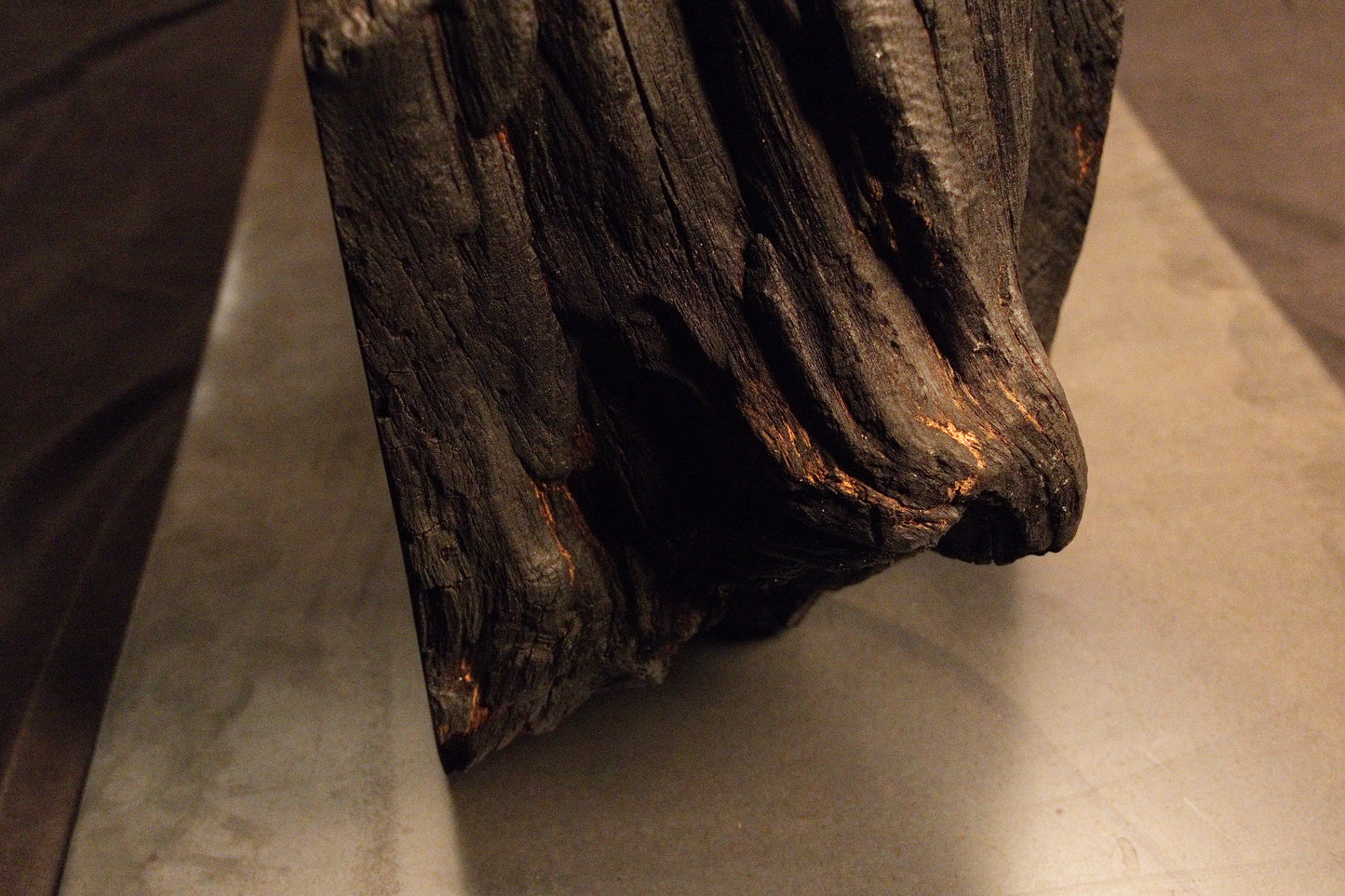 Side perspective of a heavily textured, dark weathered root section resting securely upon a sleek metallic base plate.  
