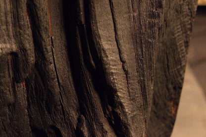 Deep vertical furrows and heavily charred rustic wood texturing run continuously along the weathered timber body.  