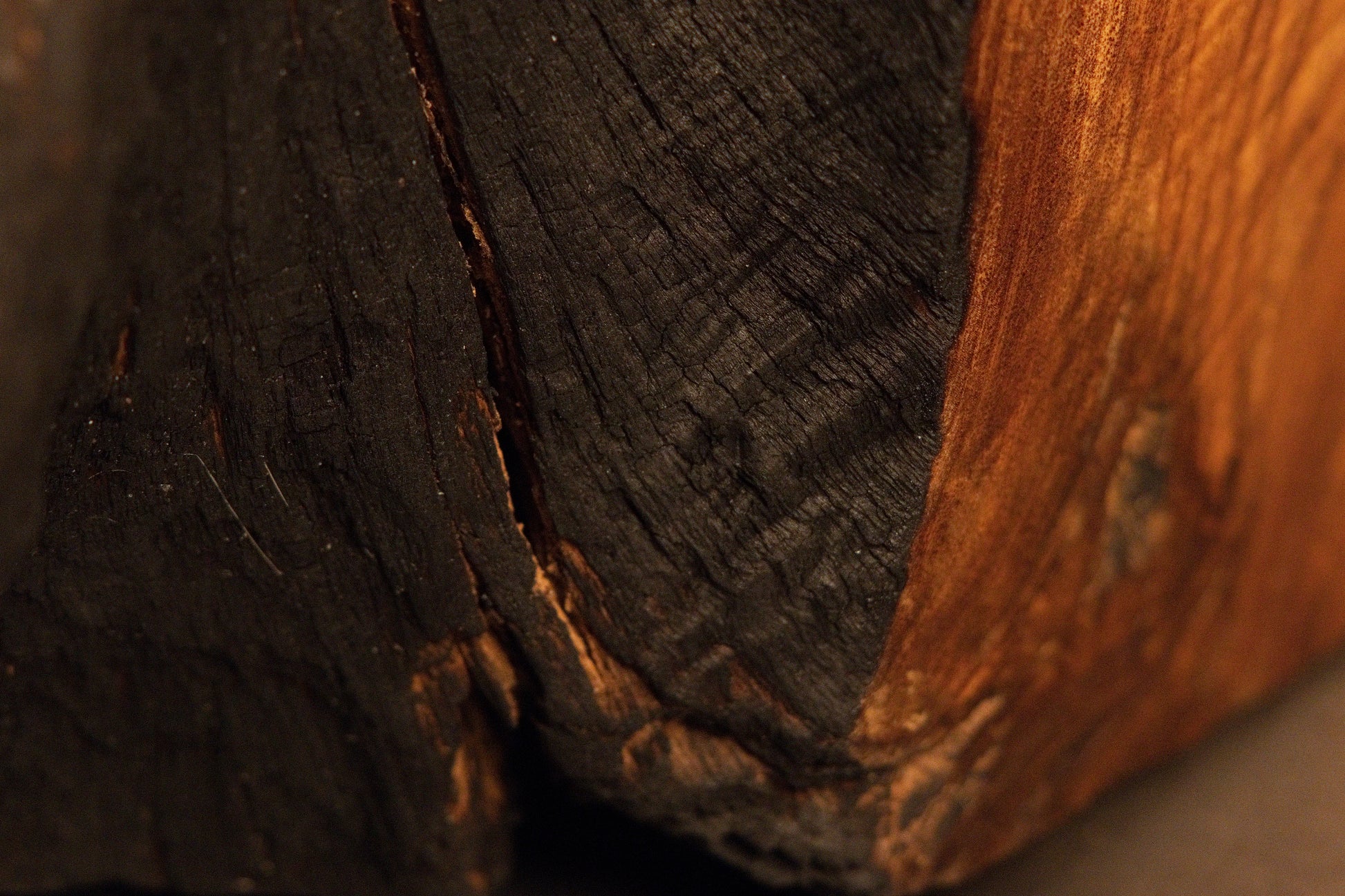 Transition zone detail where dark, heavily weathered wood texturing meets smooth, warm golden-brown surface grain.  