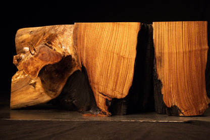 Dual-block architectural wooden bench featuring warm golden vertical grain patterns and dark charred interior void faces.  