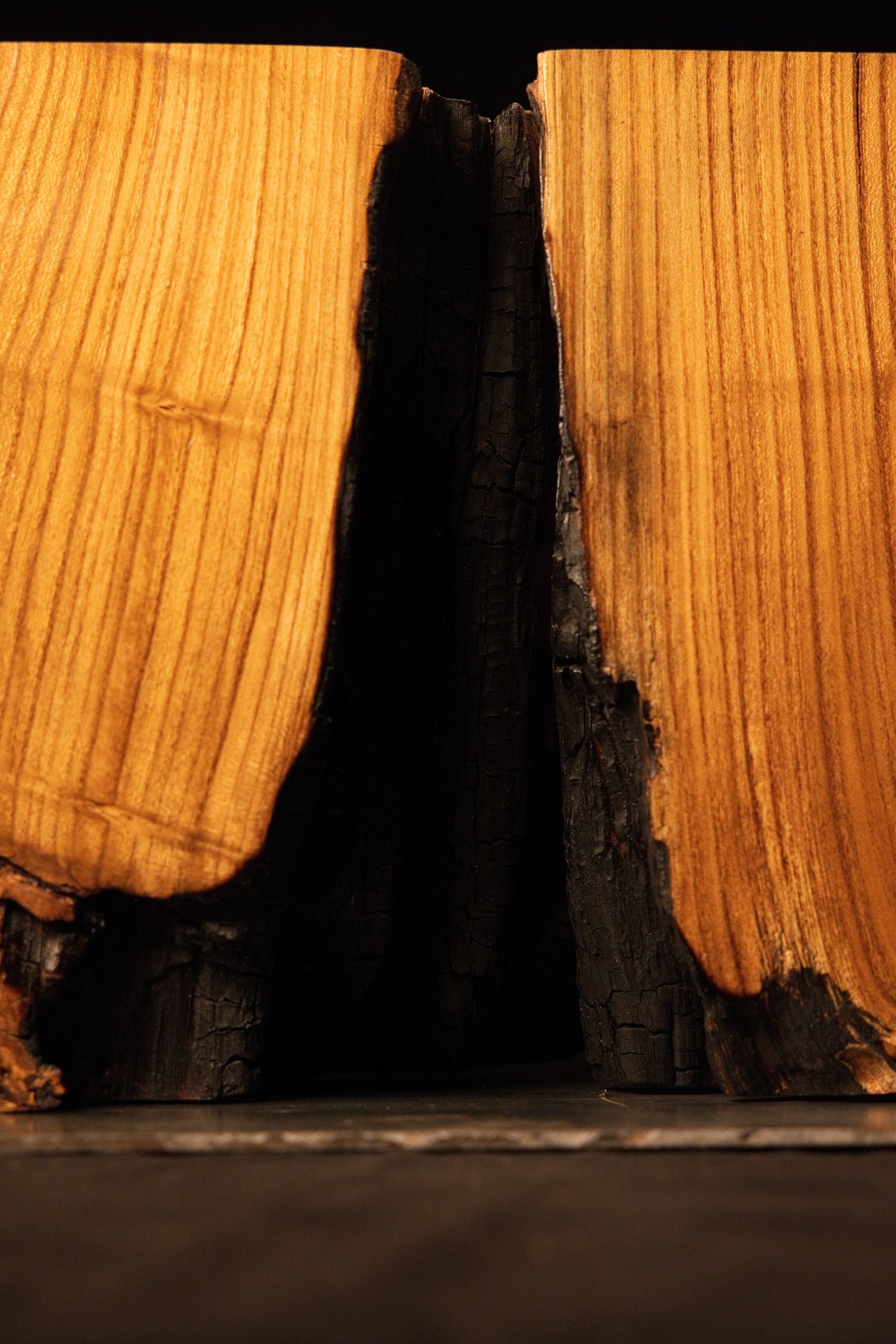 A dark charcoal-toned gap cleanly separates two precision-cut structural blocks forming a massive wooden bench.  