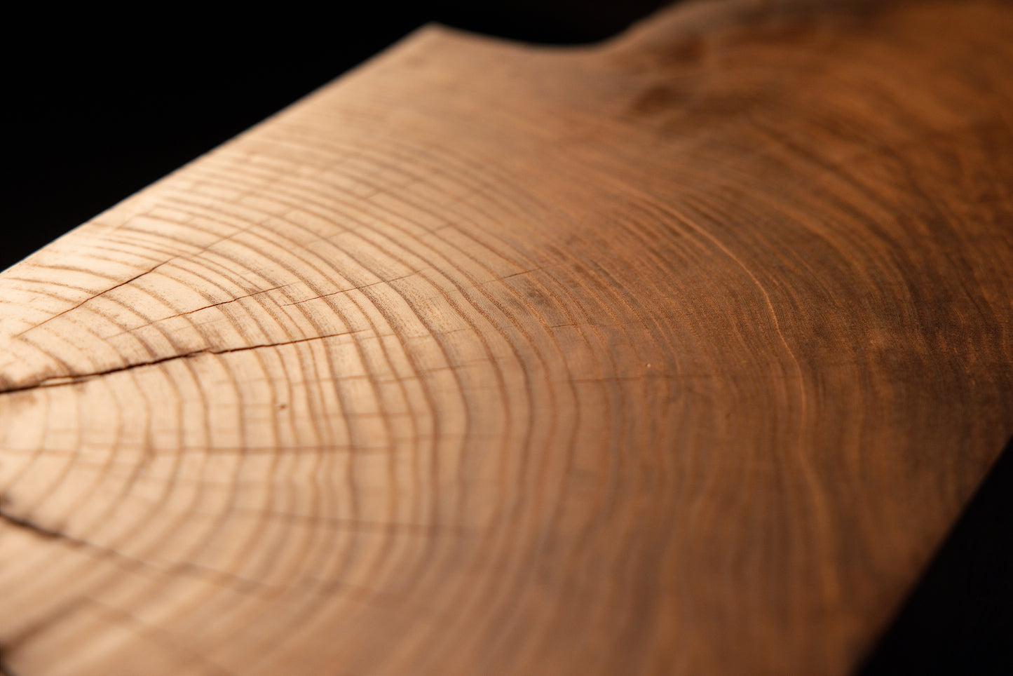 Smooth, polished growth rings run continuously along the rounded top edge of a solid square architectural block.  