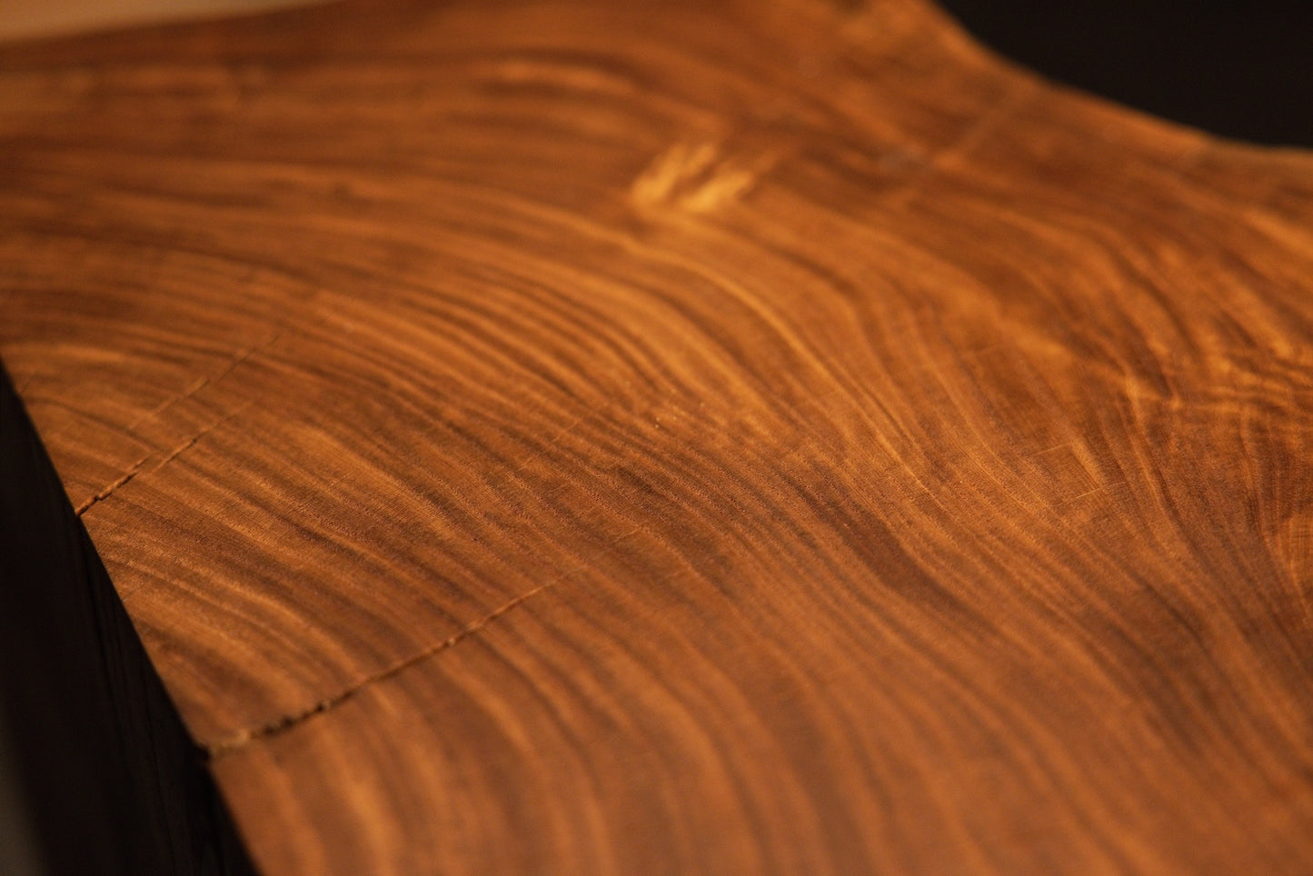 High-magnification capture of shimmering chatoyant light reflections and complex swirling grain across the wooden plane. 