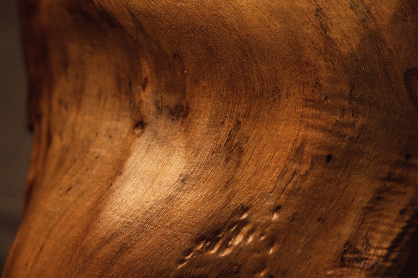 Detailed macro capture of rippling wavy grain patterns flowing smoothly across the warm curved custom wood sculpture. 