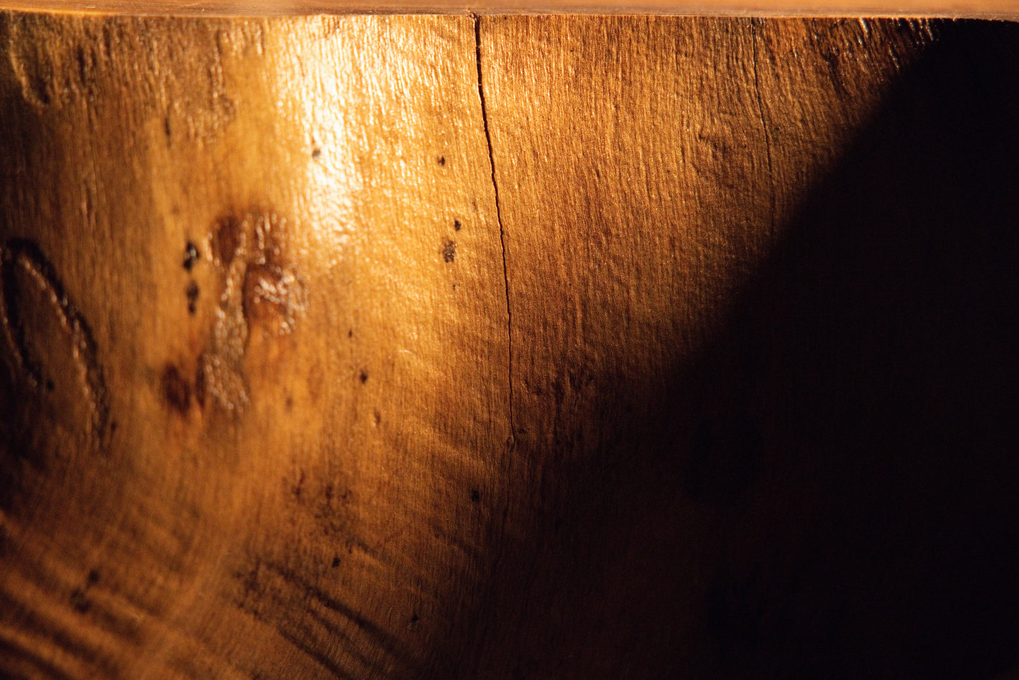 Close-up inspection of a fine vertical split line and small dark organic knot markings on a polished timber surface. 