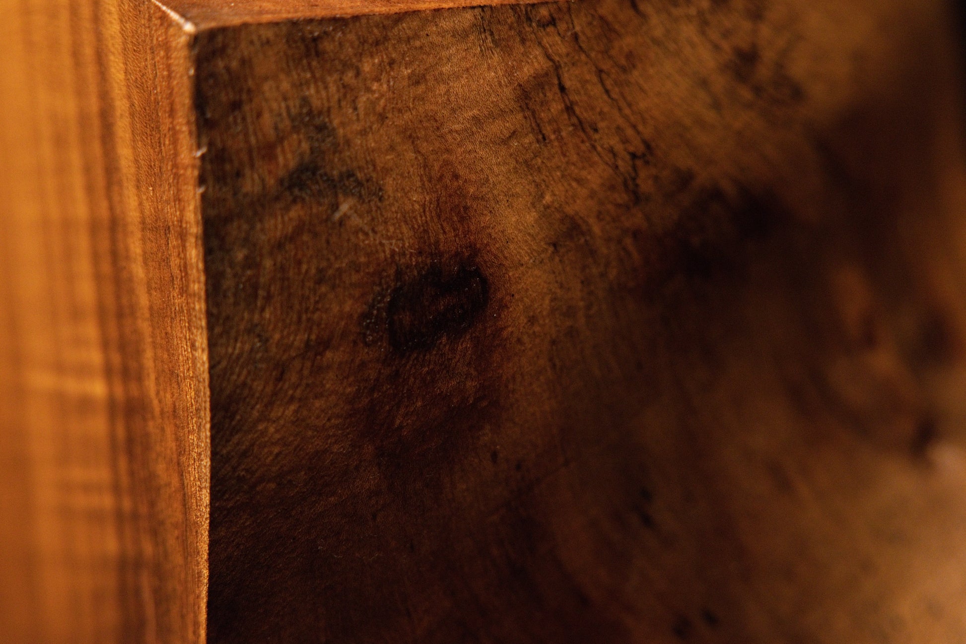 Detailed macro view capturing rich golden wood grain patterns flowing smoothly around a dark shadowed corner piece. 