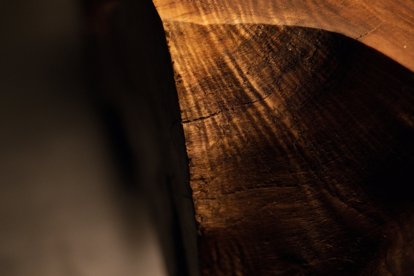 Detailed macro view capturing a dark weathered timber surface merging into deep recessed structural shadows on art. 