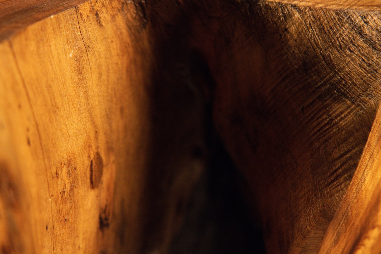 Detailed close-up macro view of natural wood grain flowing smoothly toward a dark shadowed recess on the furniture. 