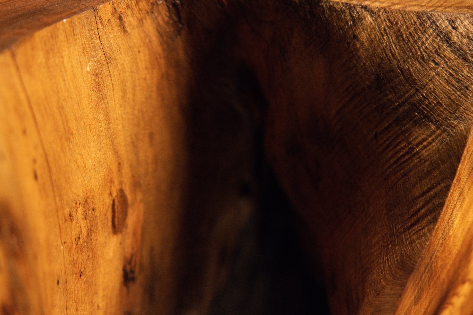 Detailed close-up macro view of natural wood grain flowing smoothly toward a dark shadowed recess on the furniture. 